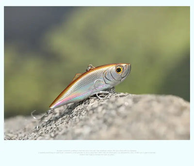 Fishing lure, orange and silver minnow with treble hooks on rocky surface