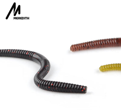 Curled black silicone worm bait lure with red speckles, other baits partly visible