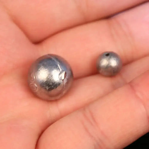 Dark gray round lead ball sinker with small hole, held in a hand for scale