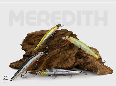 Multiple minnow fishing lures with realistic scales on driftwood, treble hooks