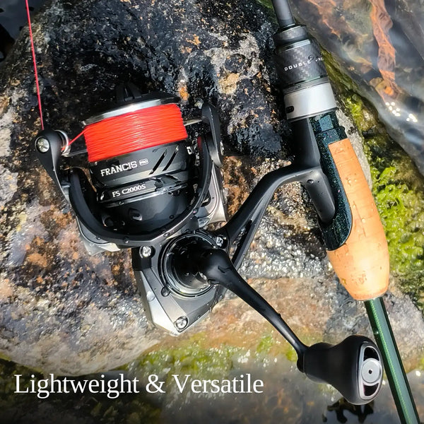 Compact spinning reel with red line spool and black handle on rocky fishing setup