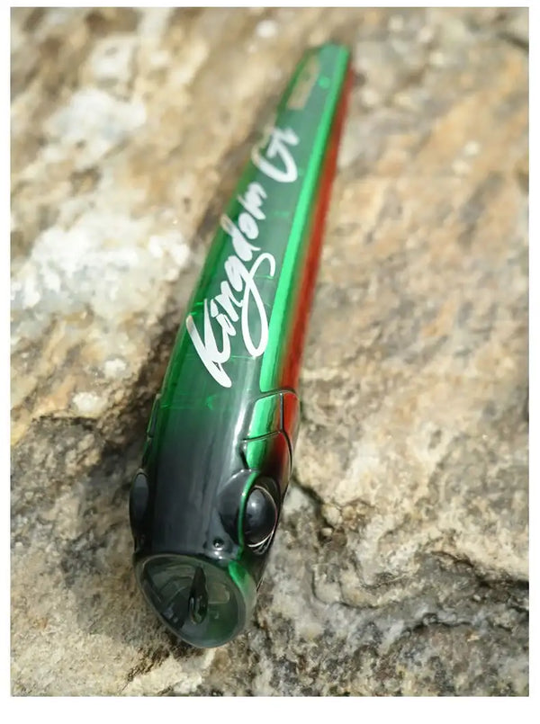 Dark green topwater popper lure with red stripe and black eye on rocks