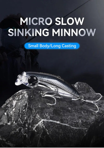Micro slow-sinking minnow fishing lure with black eye and treble hooks on rocks