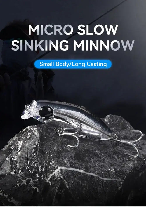 Micro slow-sinking minnow fishing lure with black eye and treble hooks on rocks