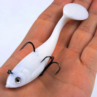 White soft fishing lure with treble hooks, held on an open palm