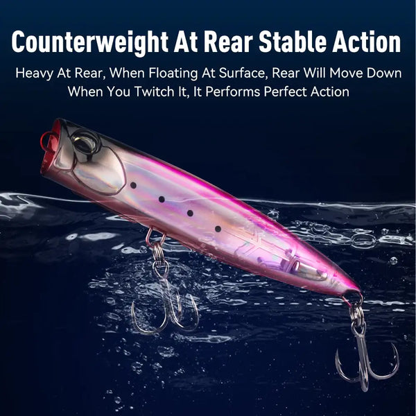 Floating popper fishing lure, pink-purple body with black dots, red front cup, splashing water