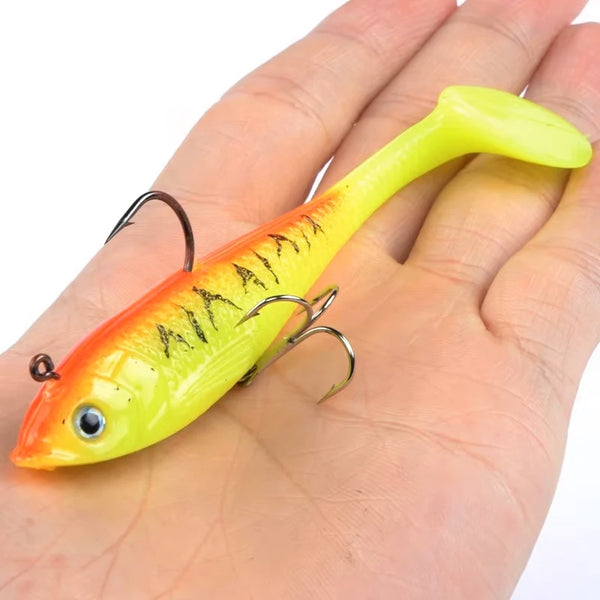 Luminous yellow/orange fishing lure with treble hooks, held on an open palm