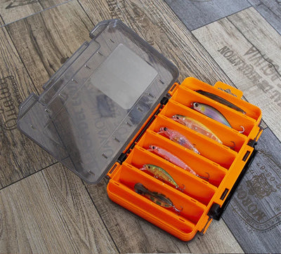 Orange double-sided tackle box open on gray floor with compartments and clear cover