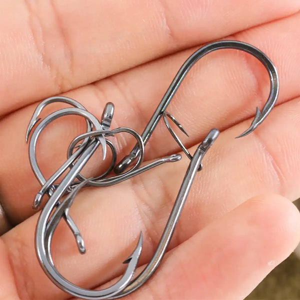 Assorted offset fishing hooks with barbs, dark metal finish, shown in hand