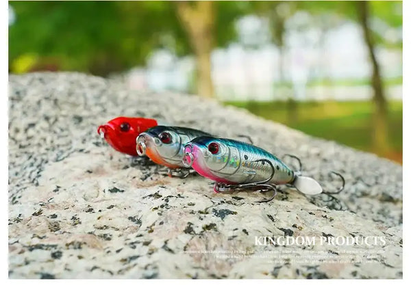Red-and-silver topwater pencil lure with rotating tail and treble hooks on a rock