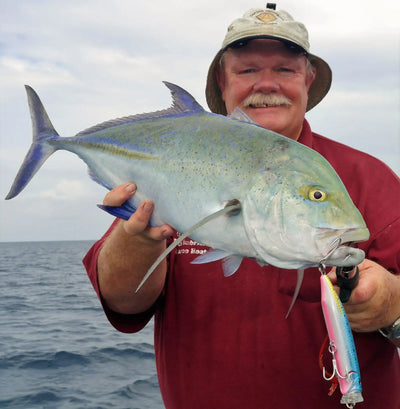 Blue and silver topwater lure held in a fish’s mouth with treble hooks attached