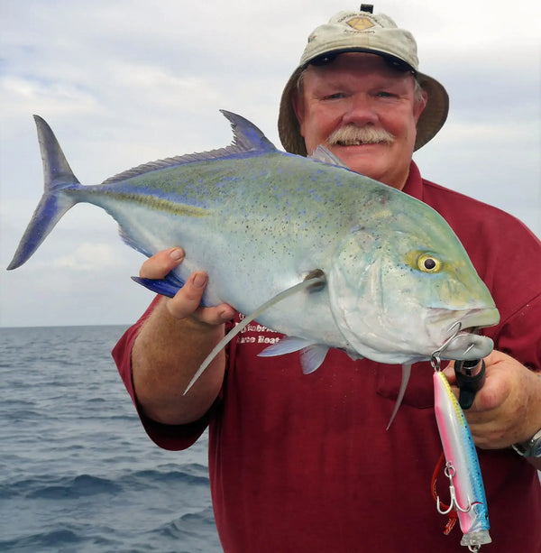 Blue and silver topwater lure held in a fish’s mouth with treble hooks attached