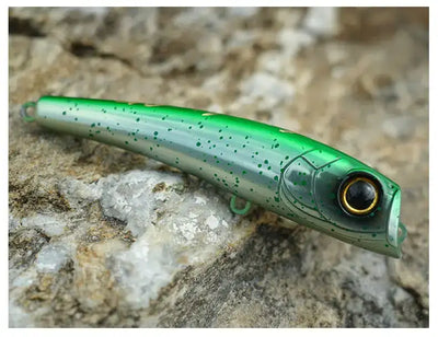 Green translucent topwater popper lure with black-tinted eye on rocks