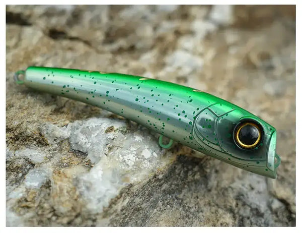 Green translucent topwater popper lure with black-tinted eye on rocks