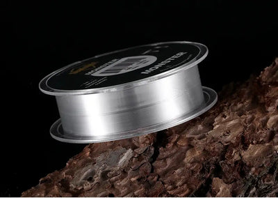 Fishing line spool in profile with MANSTER T1 label and clear line on rocky surface