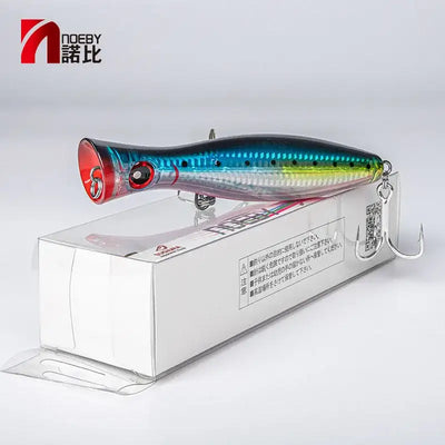 Topwater popper lure in box, blue-green body with red lip and two treble hooks