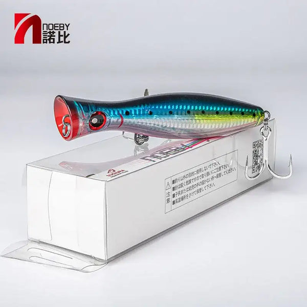 Topwater popper lure in box, blue-green body with red lip and two treble hooks