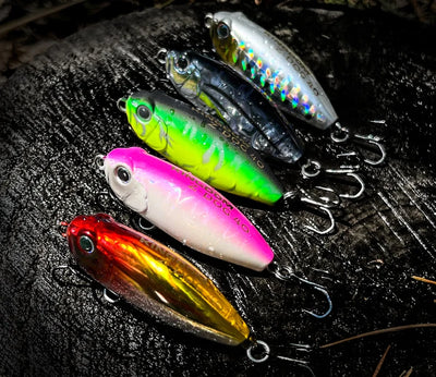 Set of floating pencil topwater lures in green, pink, and gold with treble hooks