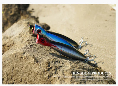 Blue and red hard artificial fishing lure on rocks with two treble hooks.