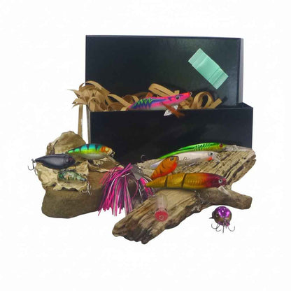 Fishing lure gift set with open black box and colorful hard body lures on driftwood