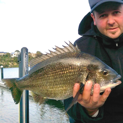 Hooded angler holding a large fish by a lakeside dock