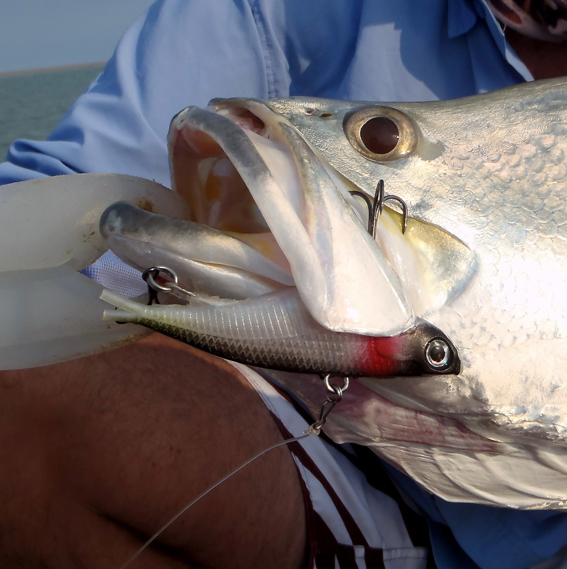 Metallic silver fishing lure with red stripe, front treble hooks and black eye detail