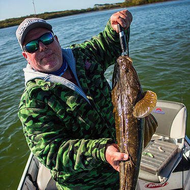 Angler wearing camo jacket and cap holding a large fish on a boat